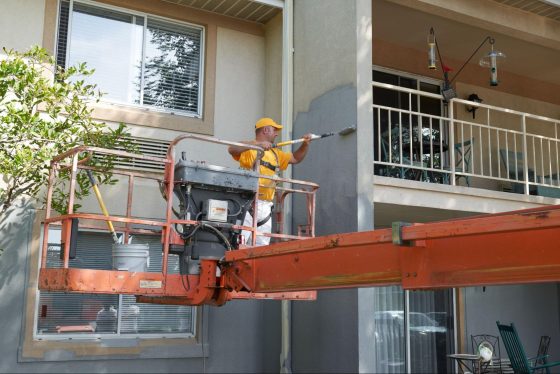 A commericial painter standing in a life to paint the exterior of an apartment building
