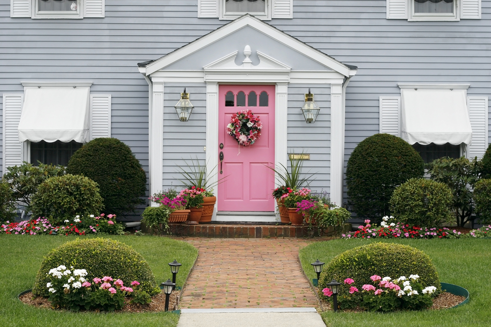 The front of a light blue home with a bright pink front door and wreath