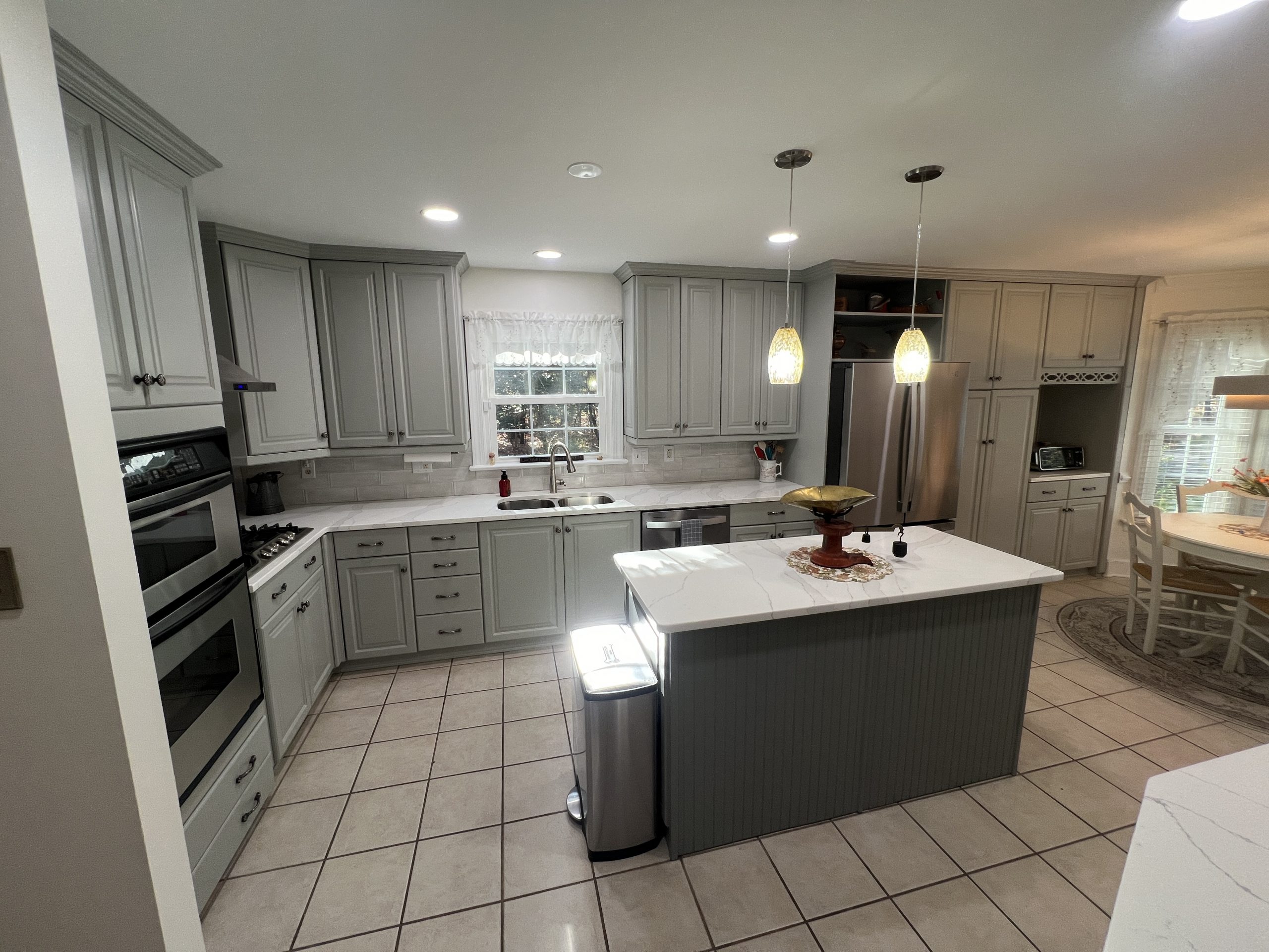 Updated kitchen in Virginia featuring sprayed soft gray raised-panel cabinets, a deeper gray beadboard island base, and light tile floors.