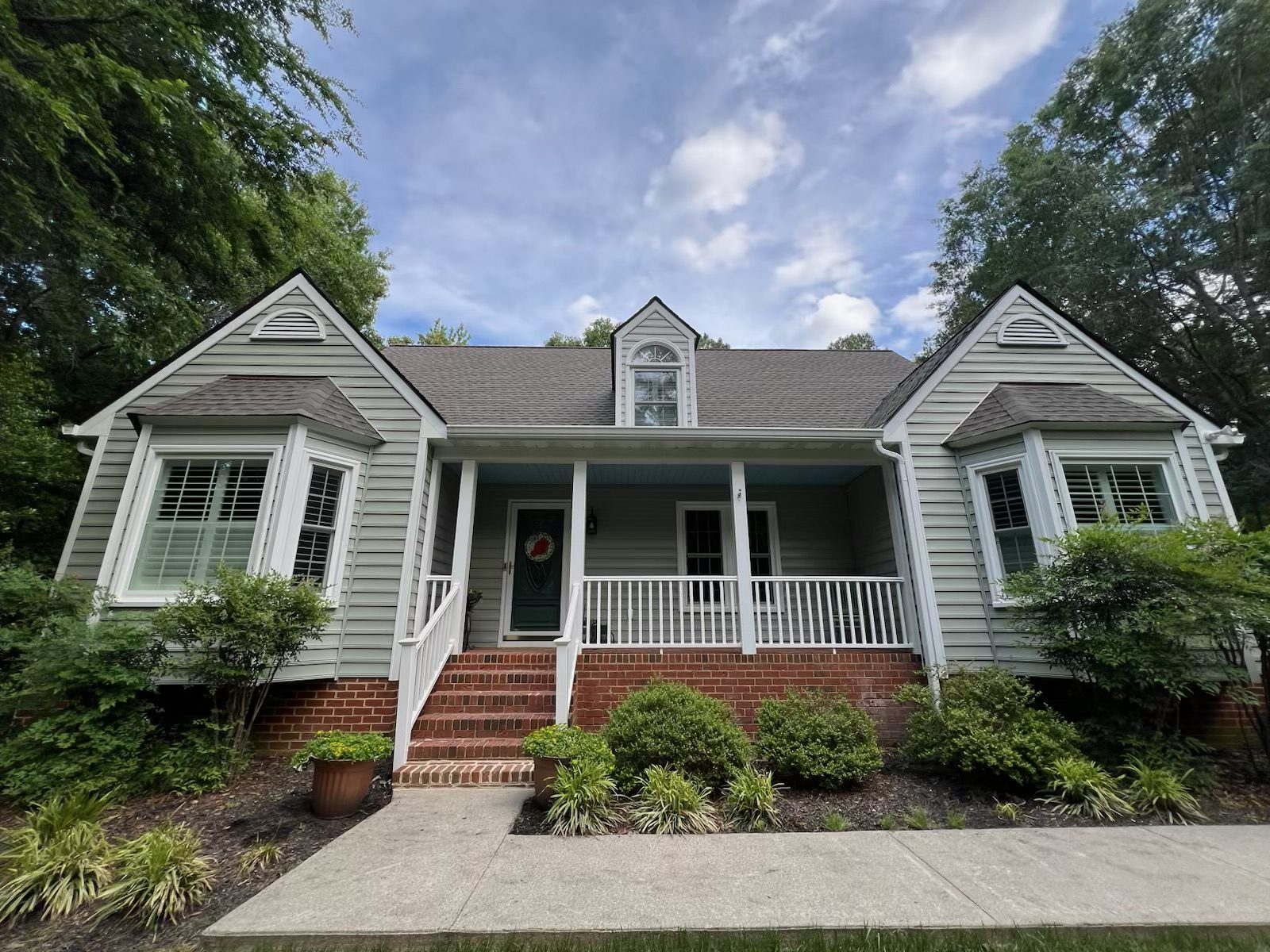 Classic Virginia home with soft gray-green siding, bright white porch railings, and natural brick foundation.