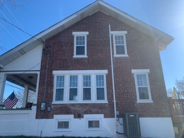 side of a brick house with white trim windows and porch