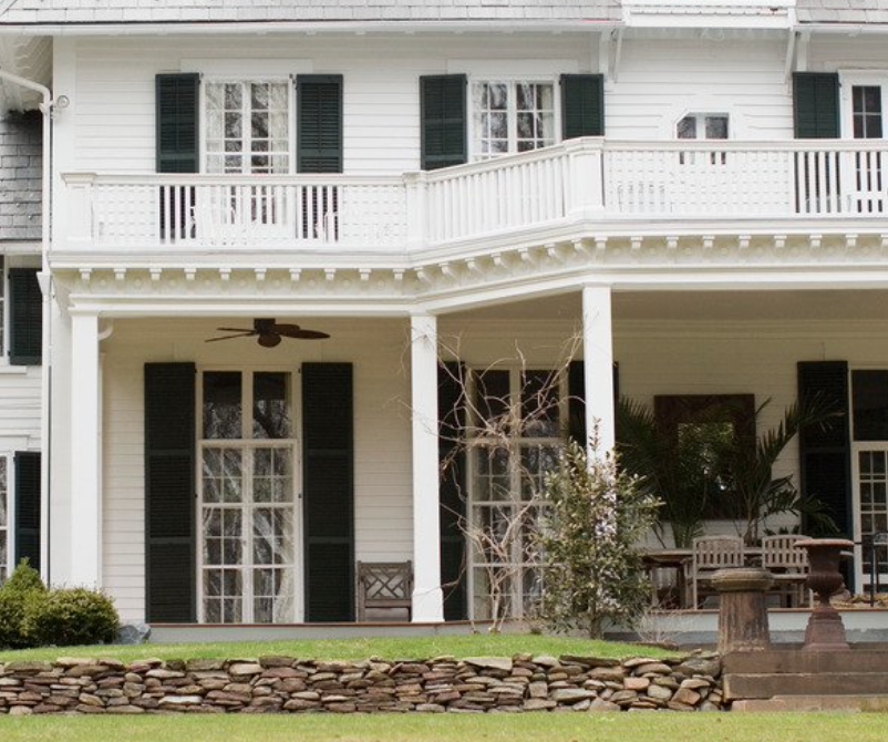 White house with black shutters and stone wall