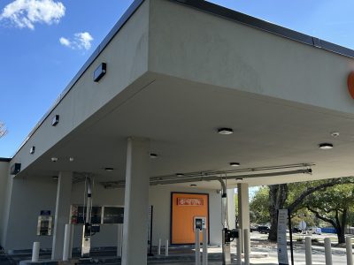 Wide view of a San Antonio bank drive-through canopy after repair and repainting, with freshly painted ceiling, support pillars, and bollards under a blue sky