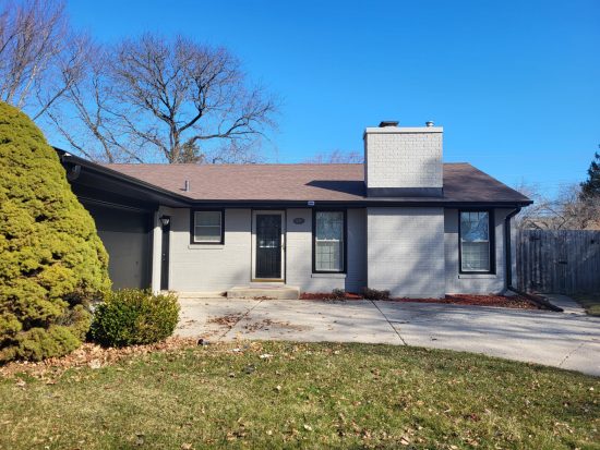 Light gray painted brick ranch home in Racine featuring black window trim, black gutters, and a black garage door.