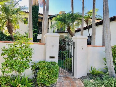 a Tile capped stucco privacy wall around a house with a wrought iron gate.