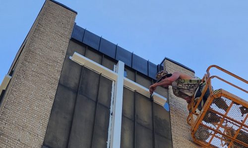painter in boom lift painting cross on church steeple