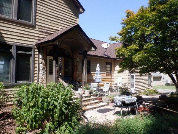 Dadeville lake house before exterior painting showing faded tan lap siding, dark brown trim, stone entry, and patio furniture Preview Image 6