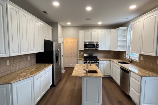 Kitchen featuring factory-smooth white raised-panel upper and lower cabinets, matching white island, and light gray walls.
