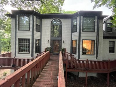 Wooded Alabama property featuring light gray exterior siding, charcoal window frames, and an elevated wood entry walkway.