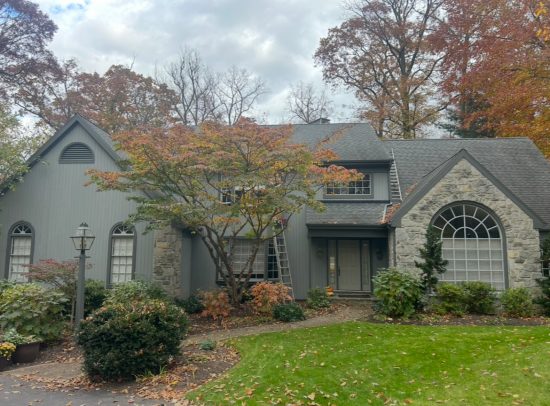 Modern Lancaster home featuring medium gray vertical board-and-batten siding, charcoal window trim, a light gray front door, and natural stone facade.