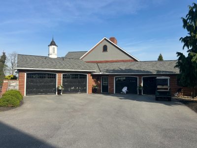 CertaPro painter applying black finish to carriage garage doors framed by white trim and a muted gray-green gable.