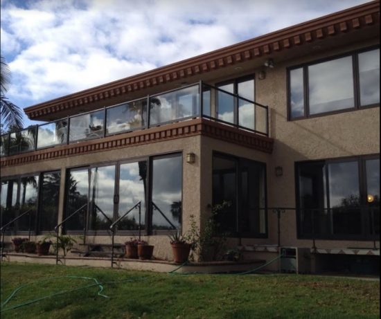Two-story Santa Monica residence with light beige stucco, dark chocolate brown eaves, brown window framing, and glass balcony railings.