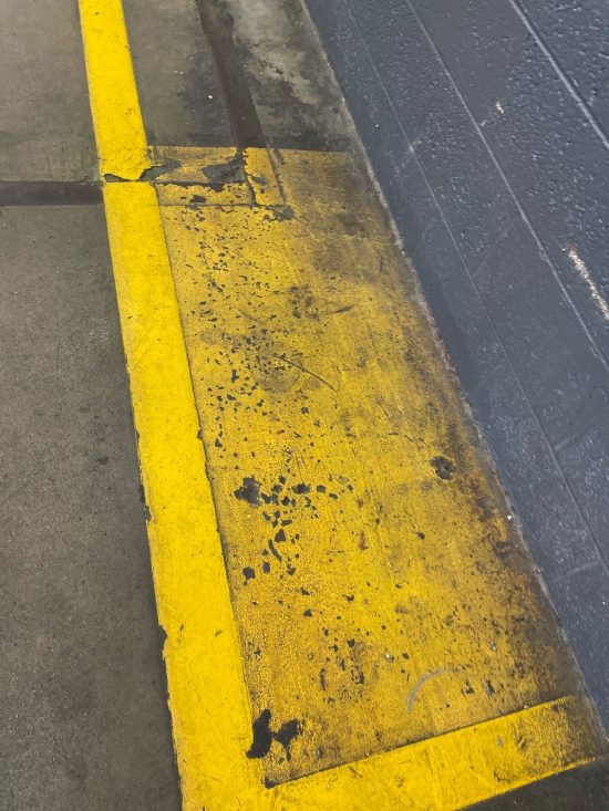 Close-up of deteriorated yellow floor coating and stained concrete before industrial floor restoration at Apex Tool Group.
