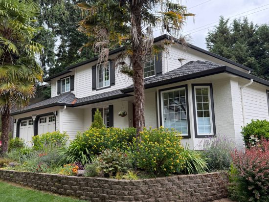 Two-story Beaverton home with white lap siding, white painted brick, deep charcoal shutters, and matching gutters.