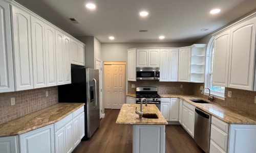 Kitchen featuring factory-smooth white raised-panel upper and lower cabinets, matching white island, and light gray walls.