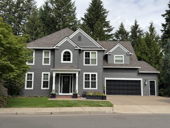 Two-story Beaverton home featuring deep charcoal gray siding, white porch columns, white trim, and solid black entry and garage doors.
