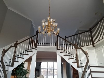 Open two-story foyer featuring light gray walls, white wainscoting, white stair balusters, and stained dark wood handrails.