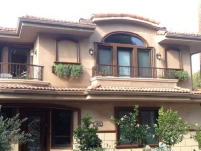Two-story Santa Monica Mediterranean stucco home with dark brown window trim, decorative wrought-iron balconies, and a red tile roof.