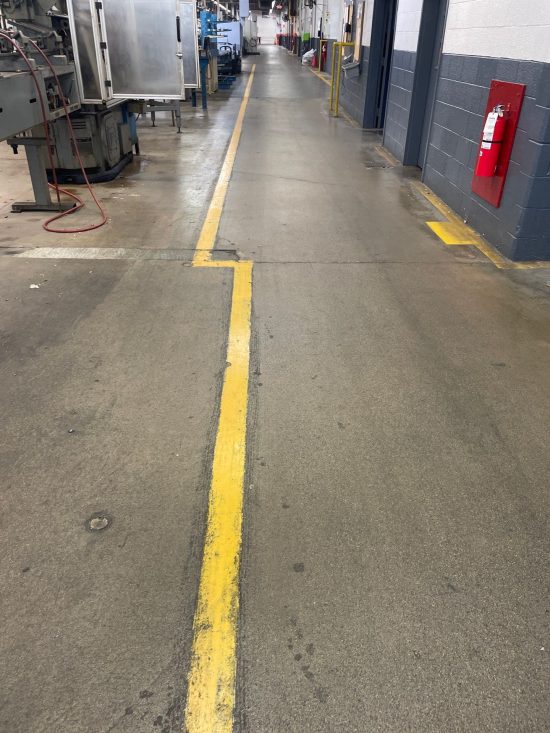 Worn concrete floor and faded yellow safety walkway markings at Apex Tool Group in Dayton, OH before epoxy floor coating.