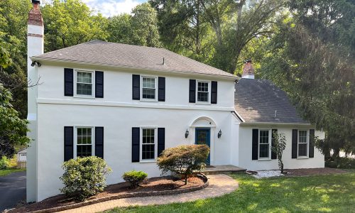 Two-story white house in Conshohocken with black window shutters, bright white window casings, and a bold blue arched front door.