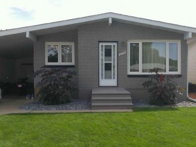 Gray painted brick ranch home showing bright white fascia and carport beams with contrasting dark windowsills.
