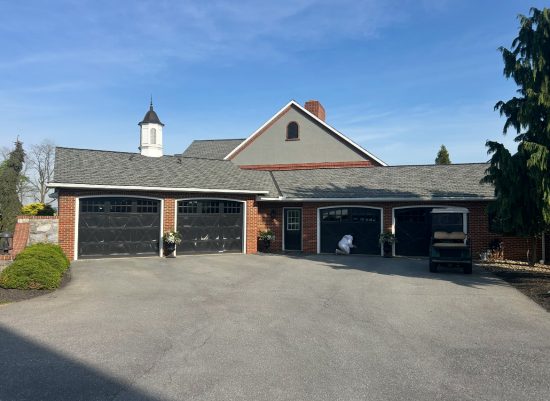 Manheim red brick garage featuring four black carriage-style doors, crisp white casing and fascia, and a medium gray gable.