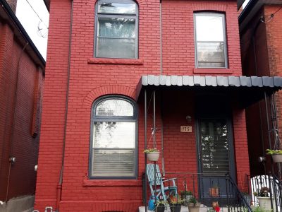 Two-story red painted brick house in Westdale with gray arched window surrounds, a gray foundation, and a dark front door.