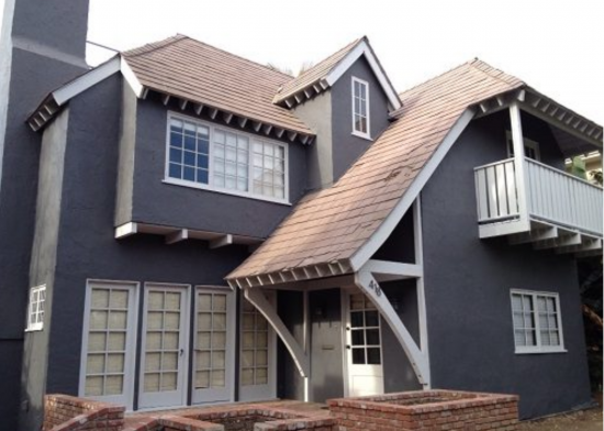 Two-story Santa Monica house featuring dark charcoal gray stucco, white rafter tails, white trim, and a white glass-pane front door.