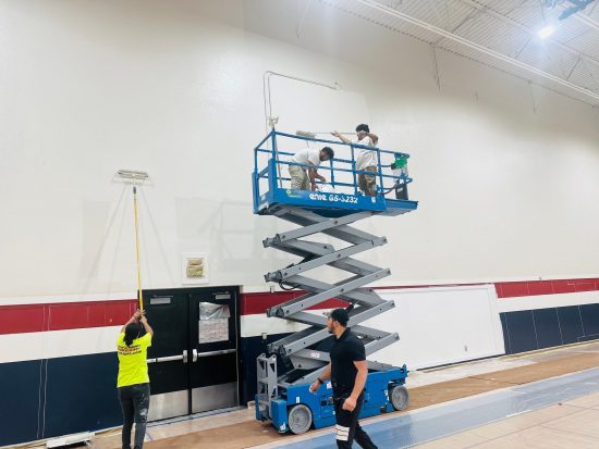 painters on scissor lift in gymnasium during repaint