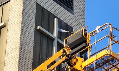 painter in boom lift power washing cross on church steeple