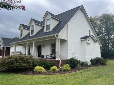 Alabama ranch house with fresh white painted brick, neutral dormer siding, white porch columns, and unpainted brick foundation steps.