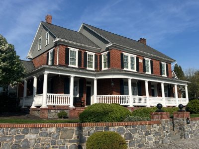 Two-story red brick colonial featuring freshly painted white wraparound porch railings, black window shutters, and gray gables.