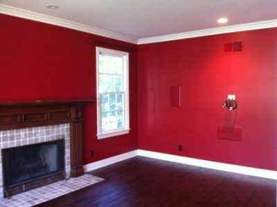 Pacific Palisades living room displaying saturated deep red walls, clean white crown molding, white baseboards, and a natural dark wood mantel.