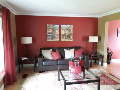 Westdale living room showcasing a deep red accent wall behind a sofa, muted olive side walls, and white crown molding.