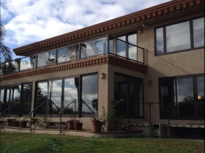 Two-story Santa Monica residence with light beige stucco, dark chocolate brown eaves, brown window framing, and glass balcony railings.