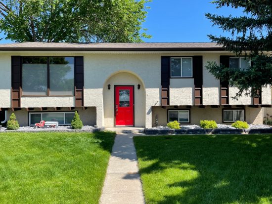 Cream stucco home with dark chocolate brown shutters, matching eaves, and a rich red front entry door.
