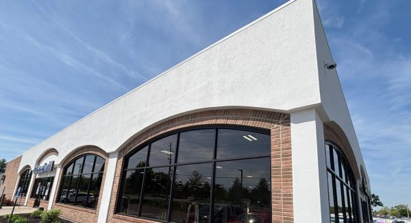 Angled finished view of white EIFS, brick arches, and storefront windows.