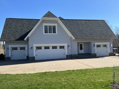 Multi-bay garage wing featuring smooth light cool-gray stucco walls, three white carriage-style garage doors, and white window surrounds.
